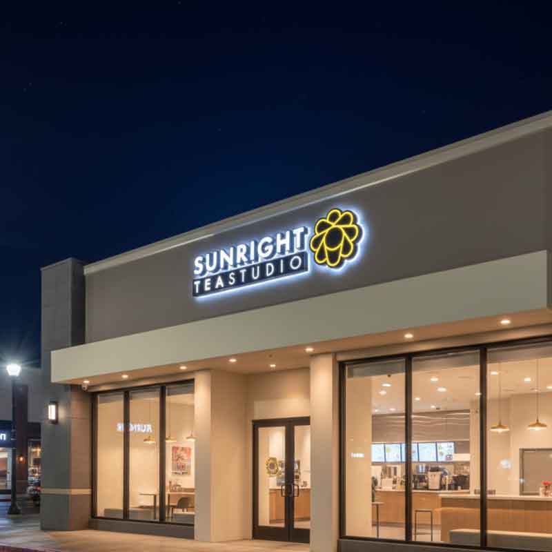 A luxury storefront with a halo-lit outdoor led sign for Sunright Tea Studio, demonstrating perfect 3000K warm-white lighting at Blue Hour.