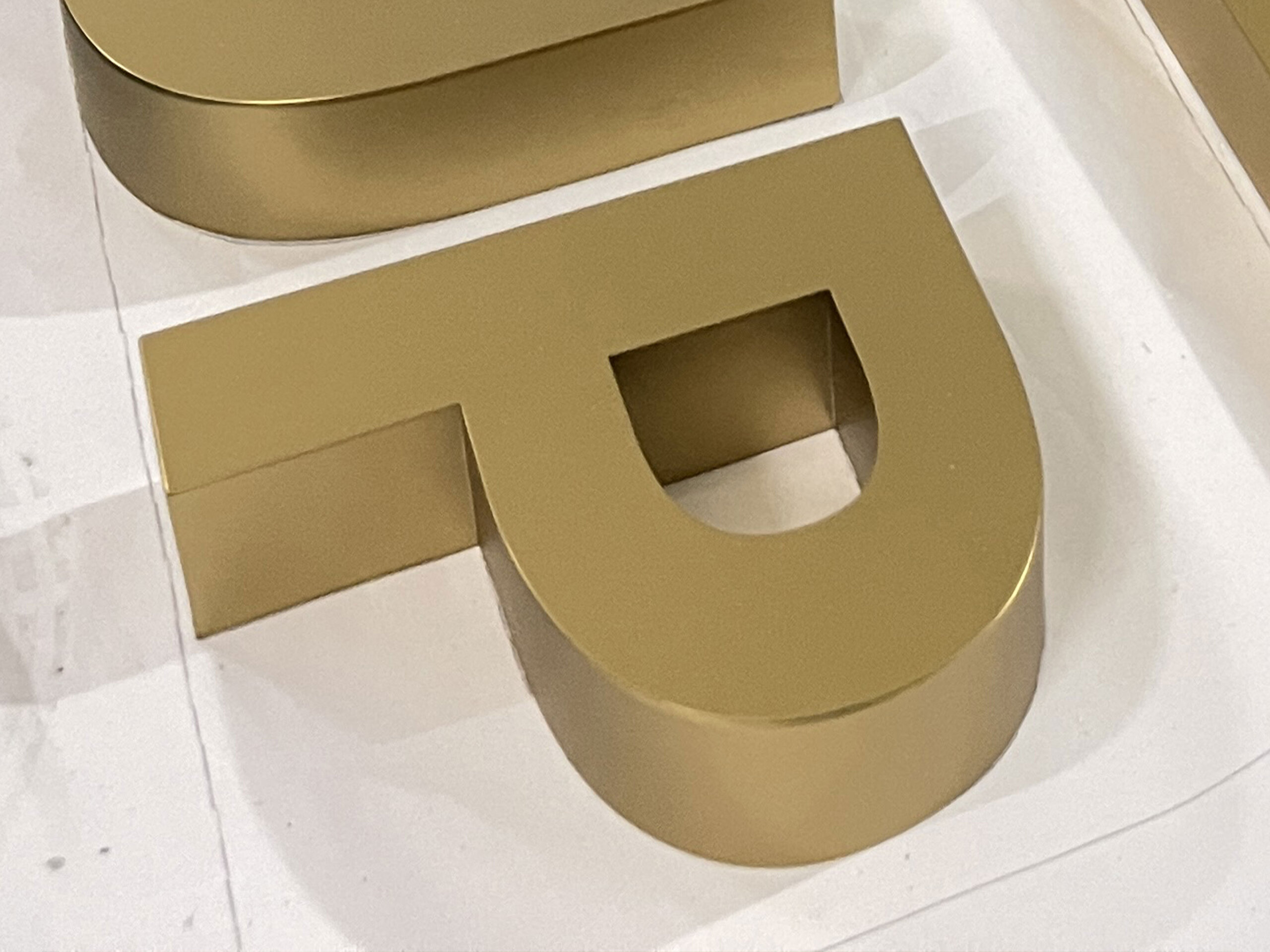 PVD matte gold stainless steel 3D lettering with a fine sandblasted finish, featuring a soft metallic glow.