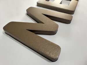 Close-up of water-plated antique bronze stainless steel lettering with a distressed (vibration) brushed finish, showing detailed surface texture.