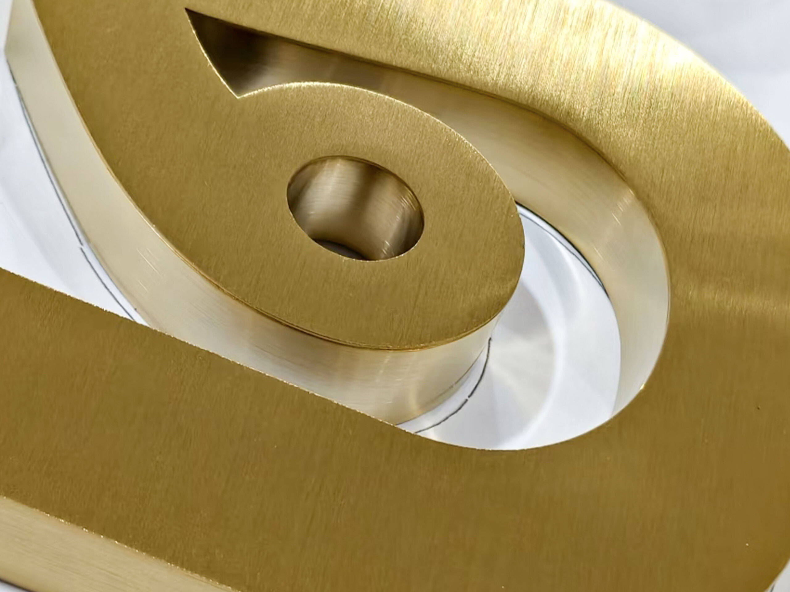 Close-up of electroplated brushed gold stainless steel 3D letters, featuring fine directional metallic hairline texture.
