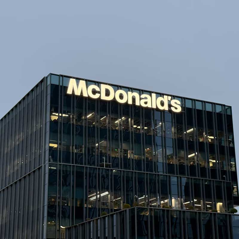 Illuminated yellow McDonald's brand signage installed on top of a modern glass-facade office building.