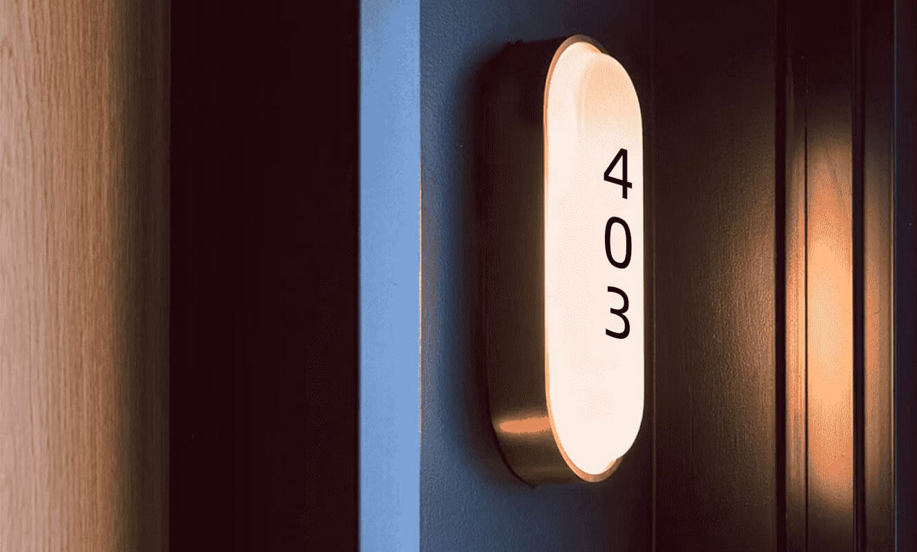 An illuminated oval room number sign displaying "403" in black text, featuring a brushed metal frame and warm white backlighting.