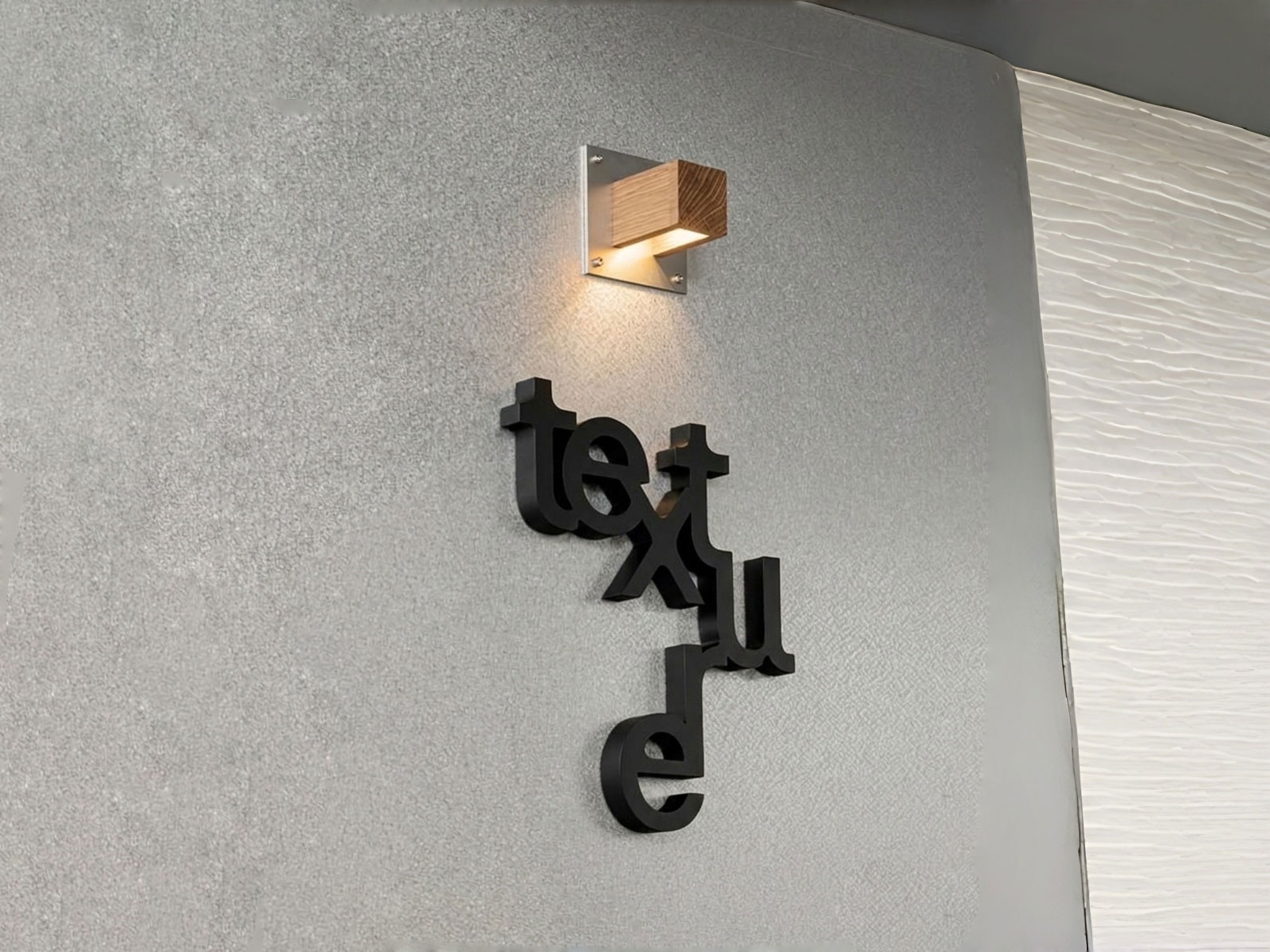 Black 3D 'texture' lettering on a grey textured wall, illuminated by a minimalist square wooden wall light casting warm shadows.
