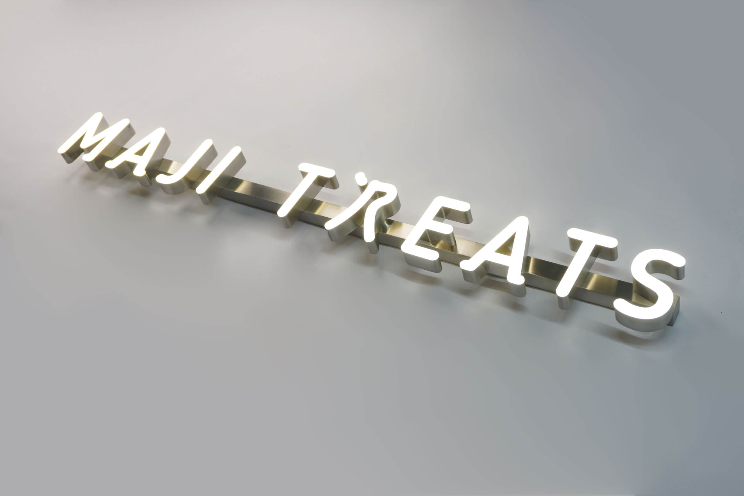 MAJI TREATS trimless hanging sign with silver metallic 3D letters, a modern minimalist suspended signage system.