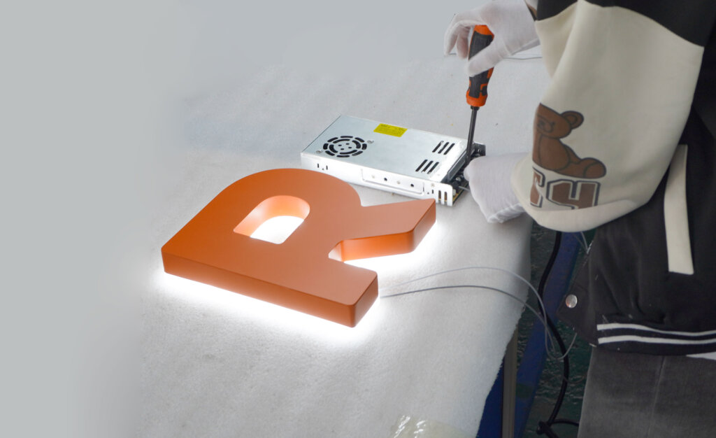 Retay·sign engineers and consultants discussing custom LED signage technical drawings and metal material samples with a client in a professional workshop setting.