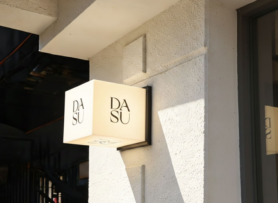 A DASU branded cube-shaped glowing light box mounted on a white stone wall, featuring a minimalist modern outdoor storefront design.