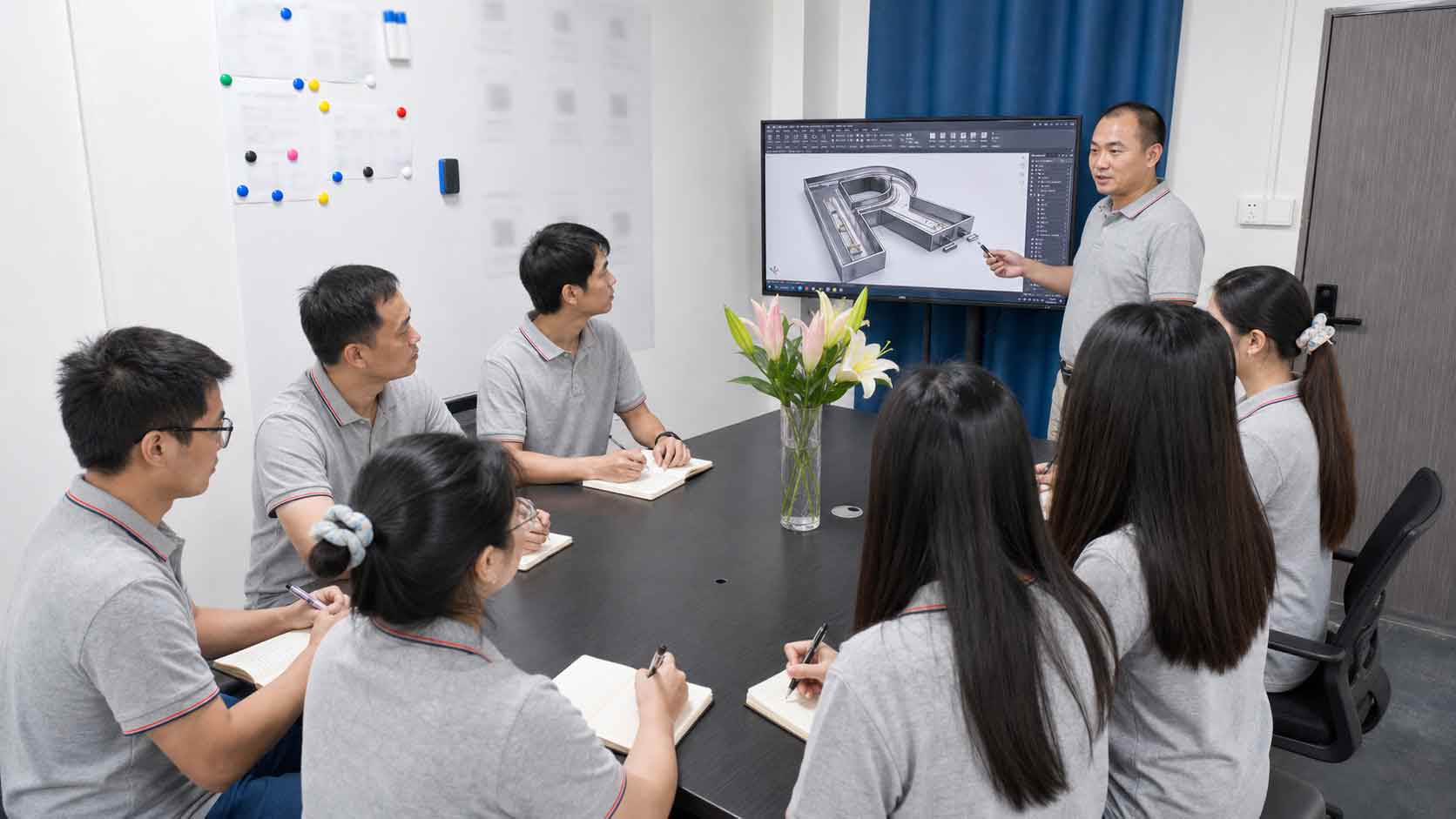 An engineer presenting a 3D CAD precision part design model to the team on a large screen.